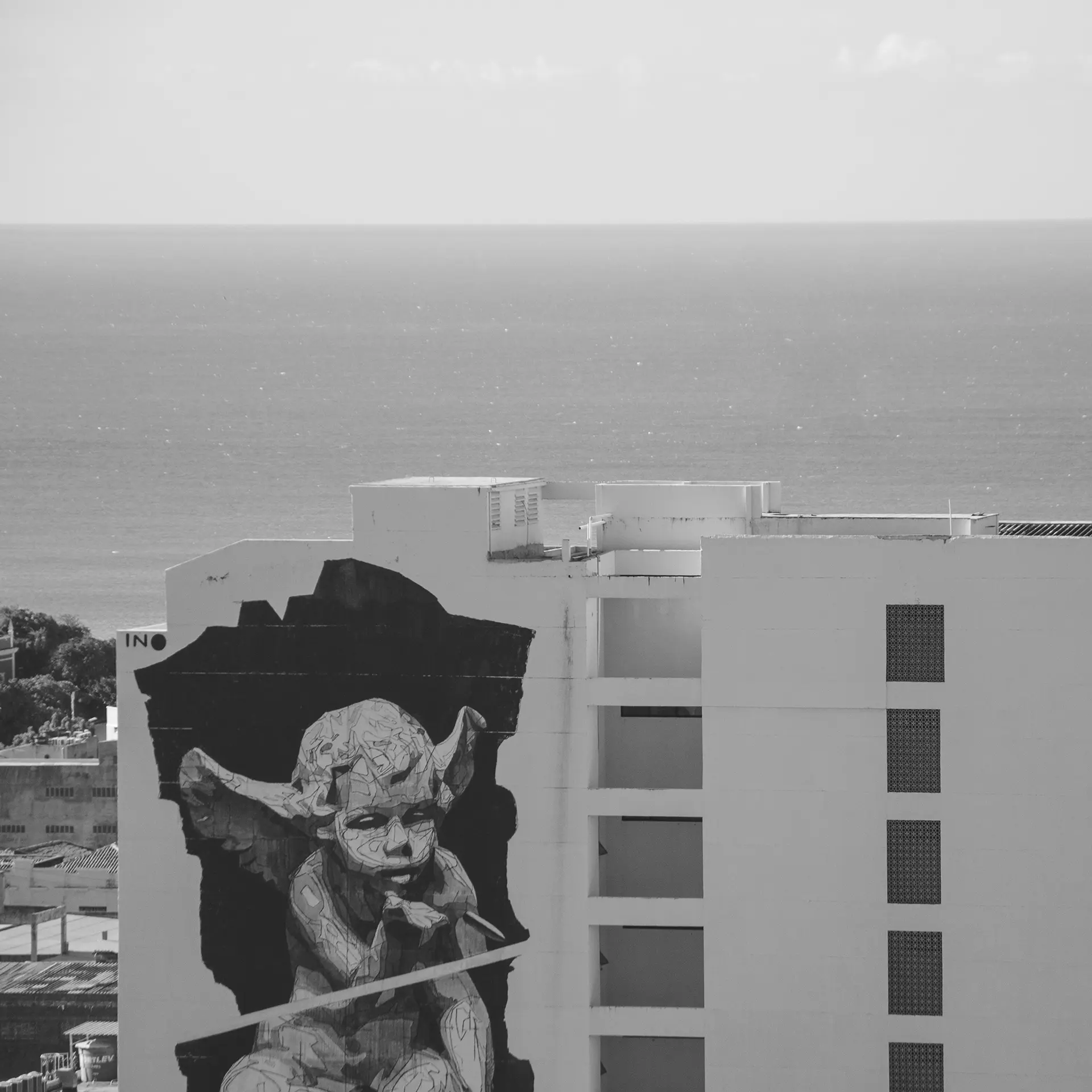 Fotografia em tons de cinza feita do alto de um prédio que mostra um gigante mural na lateral de um prédio com um anjinho assoprando uma bala no Centro de Fortaleza