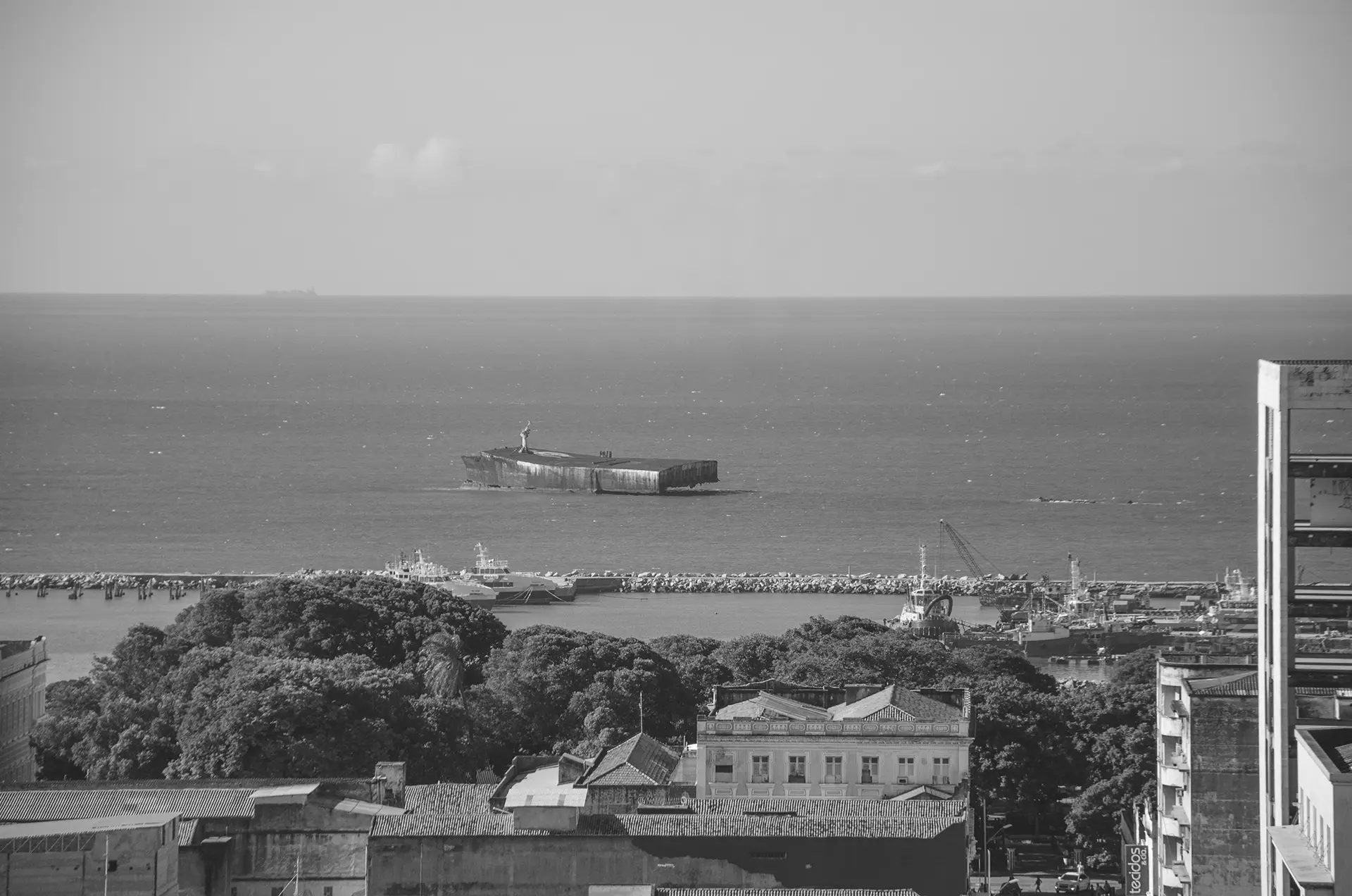 Fotografia em tons de cinza da orla de Fortaleza onde é possível observar os destroços do navio Mara Hope que havia passado por uma intervenção artística