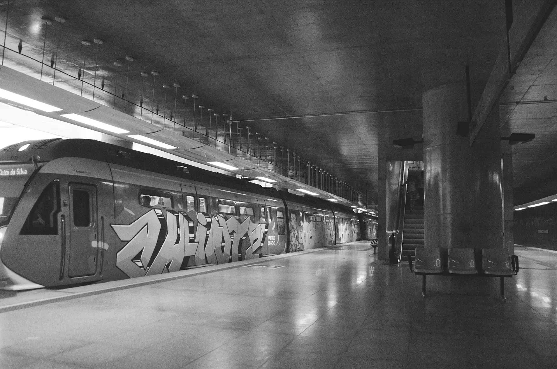 Fotografia em tons de cinza do trem todo grafitado na Estação de metrô do Benfica em Fortaleza