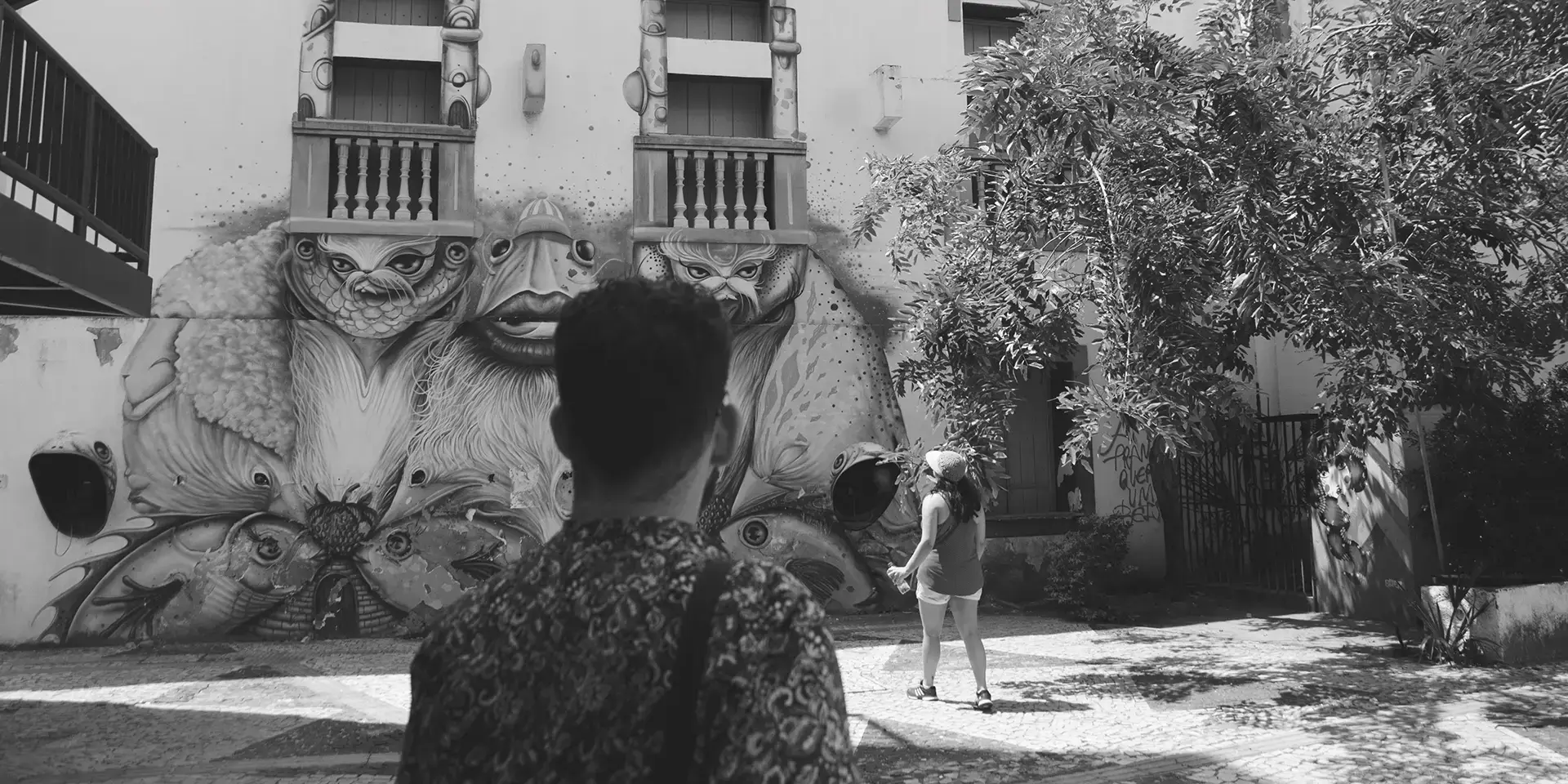 Fotografia em tons de cinza de um homem de costas olhando para um mural de graffiti no Centro Cultural Dragão do Mar de Arte e Cultura