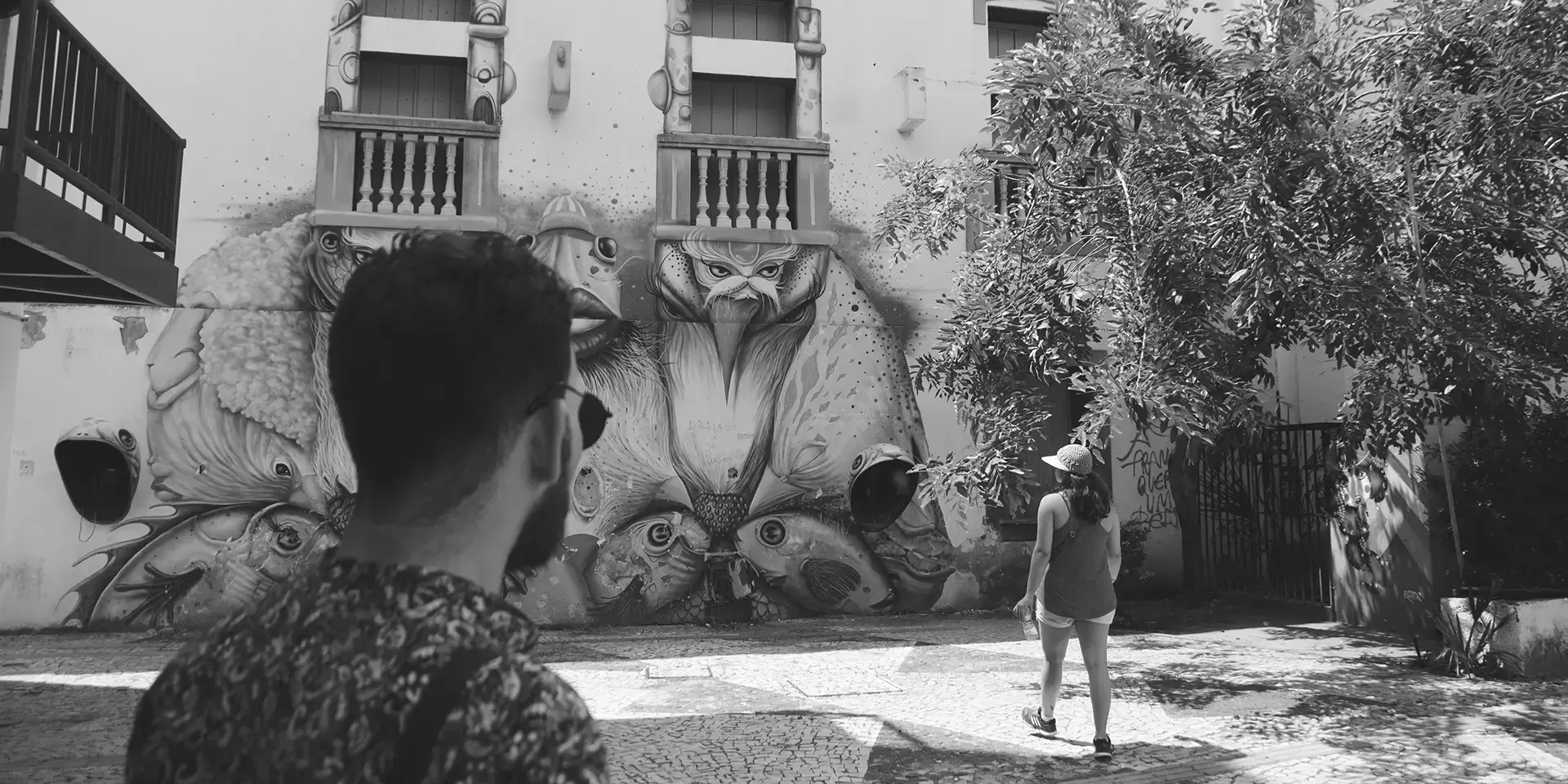 Fotografia em tons de cinza de um homem de costas olhando para um mural de graffiti no Centro Cultural Dragão do Mar de Arte e Cultura