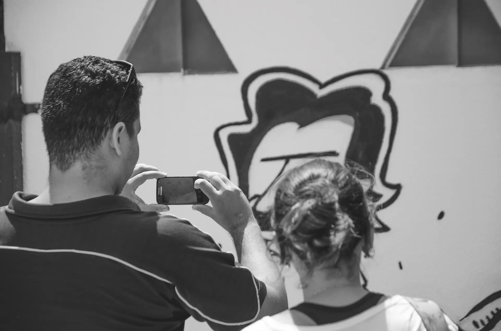Fotografia em tons de cinza de pessoas fazendo fotos com o celular em frente a um mural de graffiti