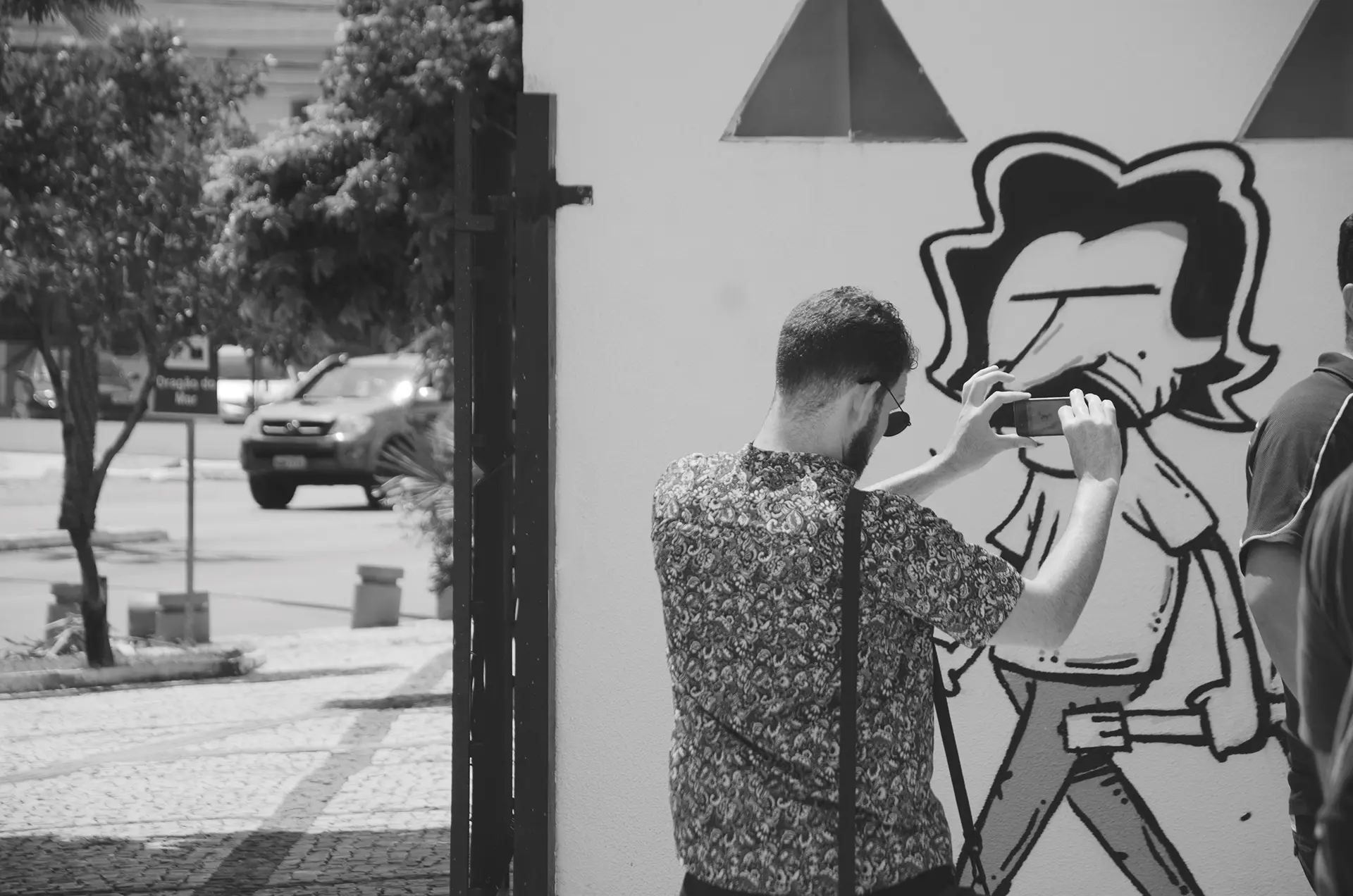 Fotografia em tons de cinza de pessoas fazendo fotos com o celular em frente a um mural de graffiti