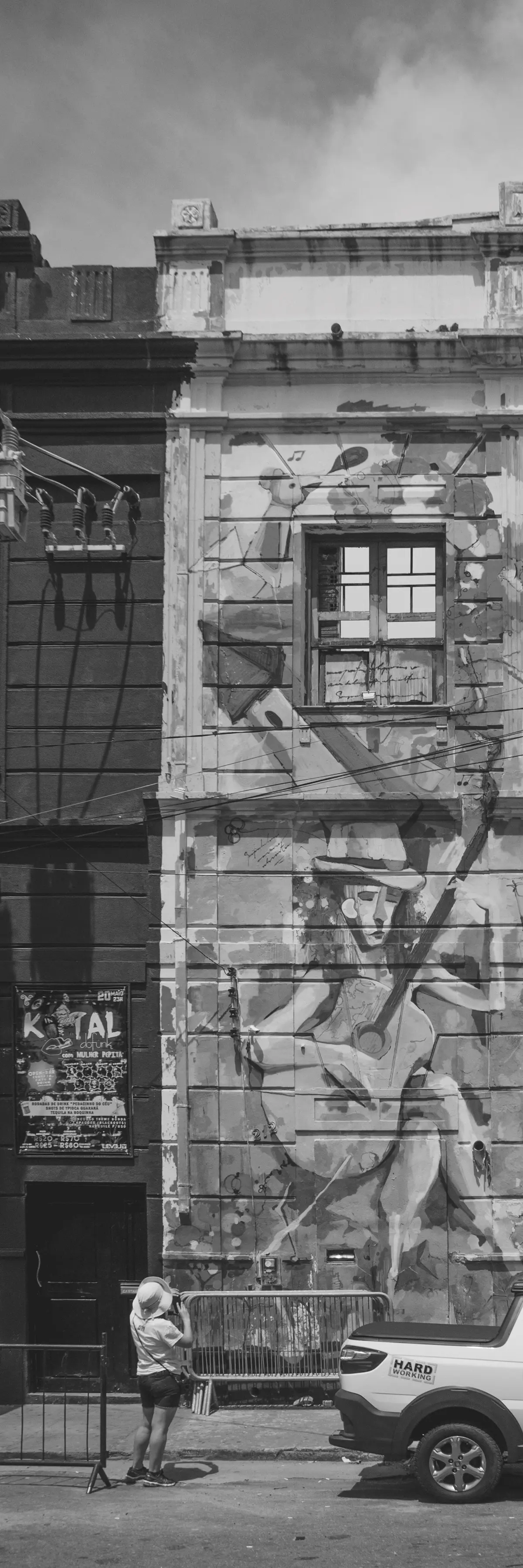Fotografia em tons de cinza de um prédio antigo todo grafitado com uma mulher de costas observando o prédio