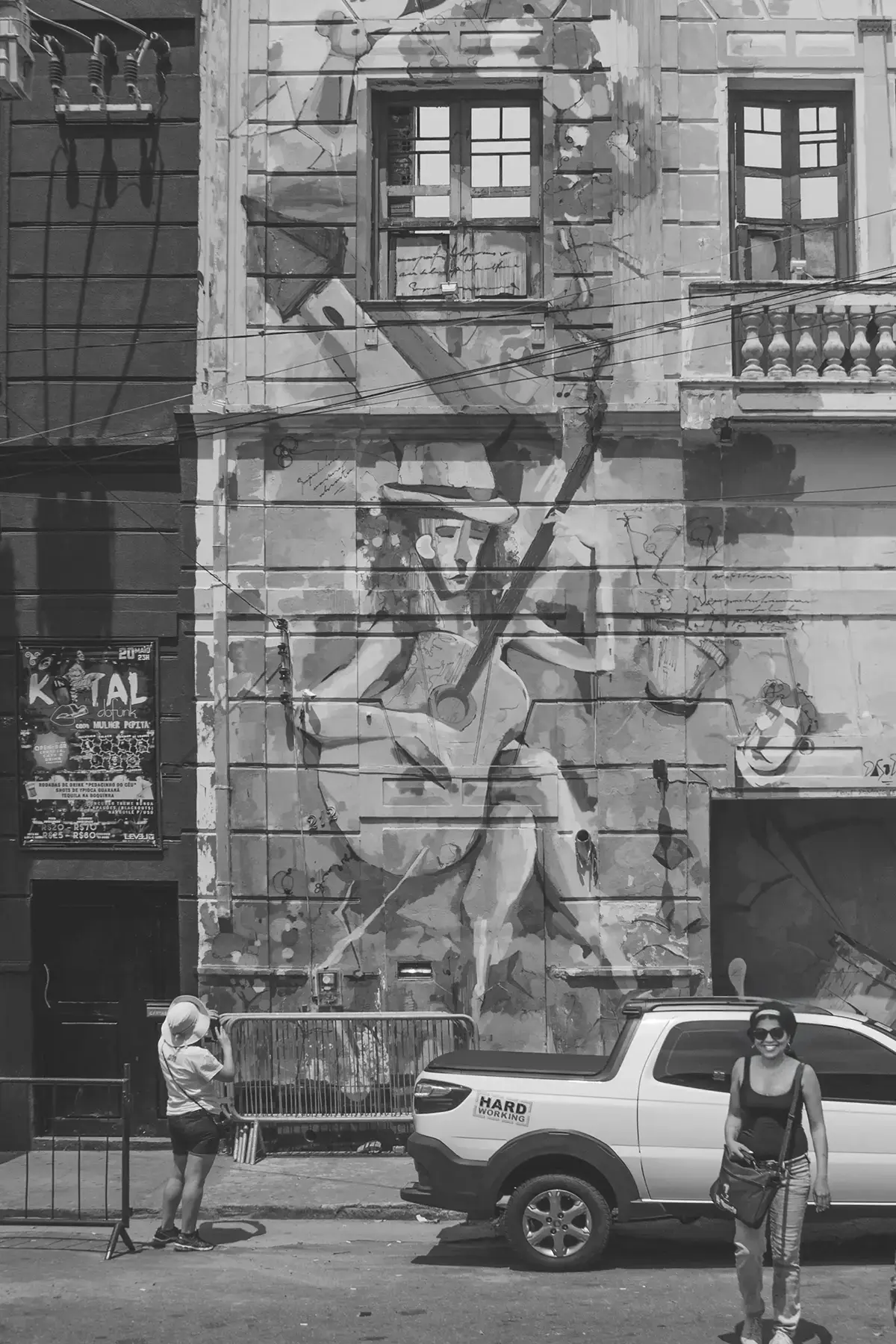 Fotografia em tons de cinza de um prédio antigo todo grafitado com uma mulher de costas observando o prédio